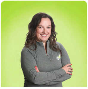 Smiling woman with dark hair crossing her arms in a gray zip-up sweater against a lime green backdrop