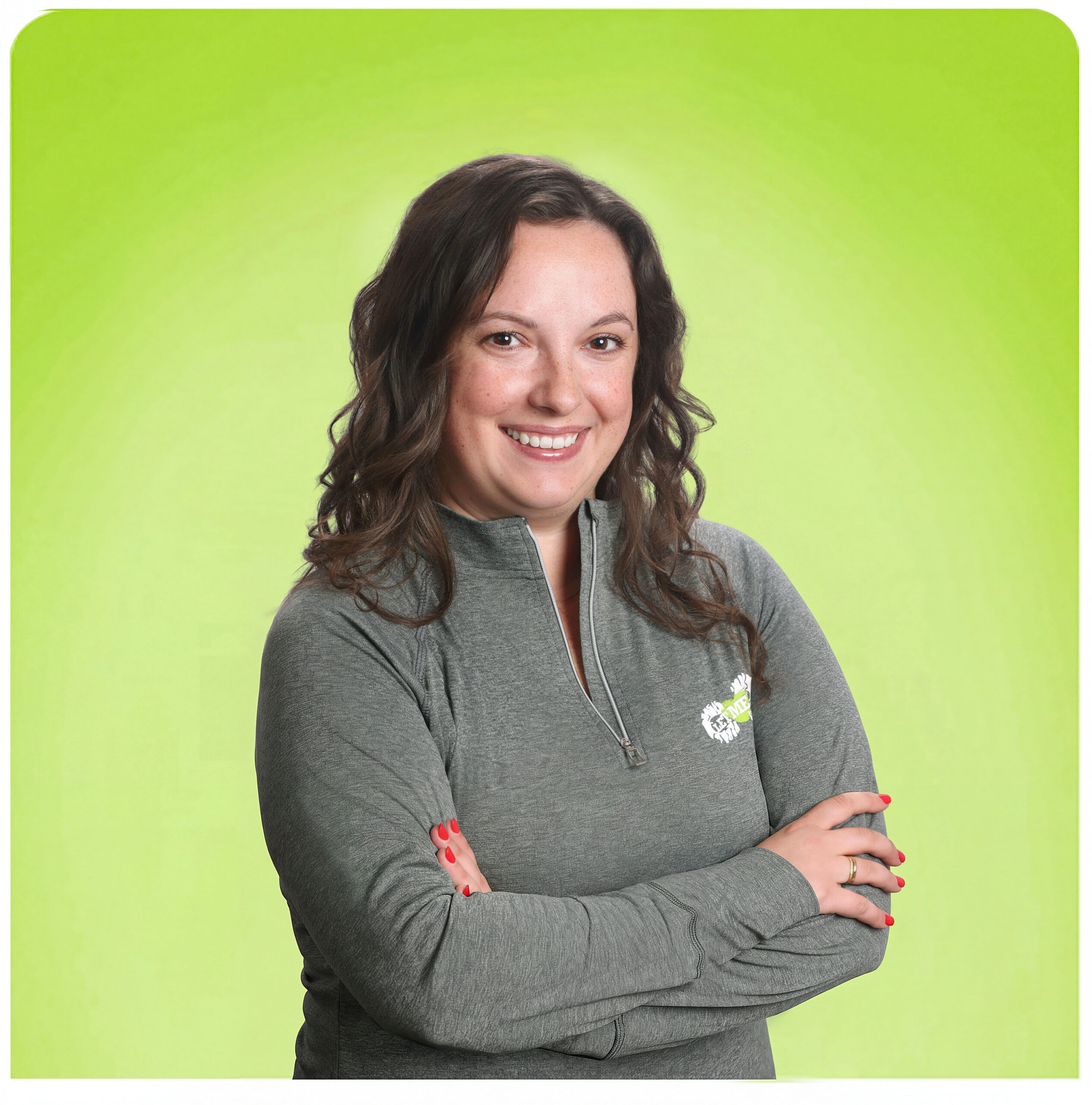 Smiling woman with dark hair crossing her arms in a gray zip-up sweater against a lime green backdrop